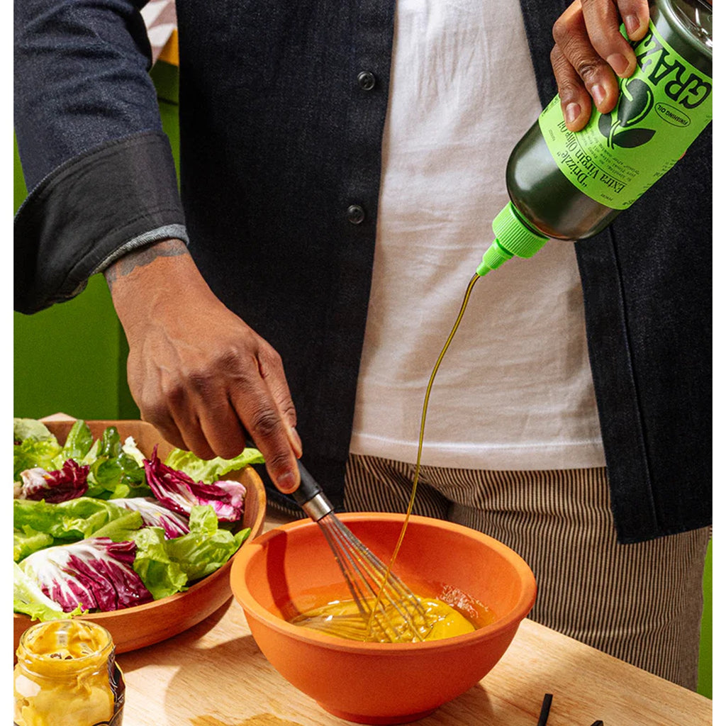 A sleek bottle of Graza Baby Drizzle olive oil, featuring a vibrant green label and a modern, ergonomic design. The olive oil is known for its rich, smooth flavor, perfect for drizzling over dishes or using as a finishing touch in cooking.