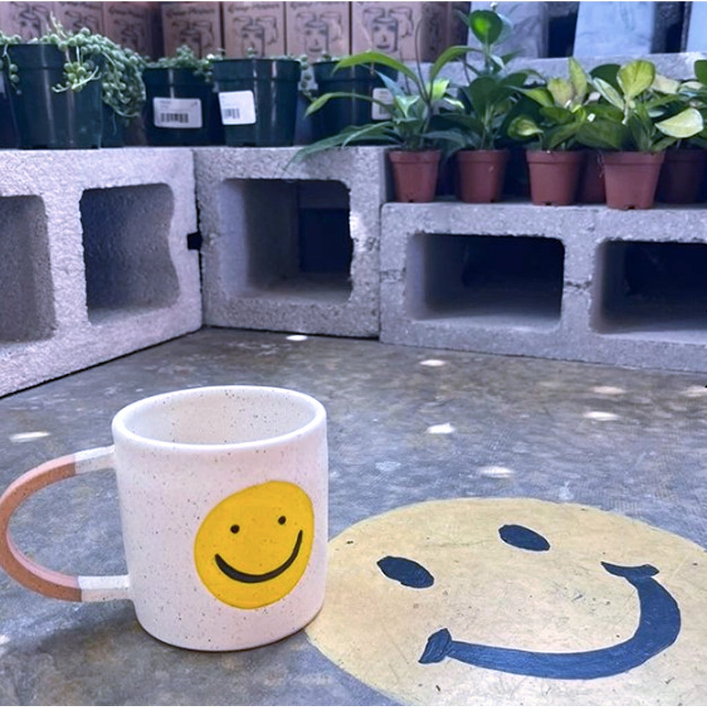 A white mug featuring a cheerful, smiling face design, perfect for adding a touch of positivity to your morning routine.