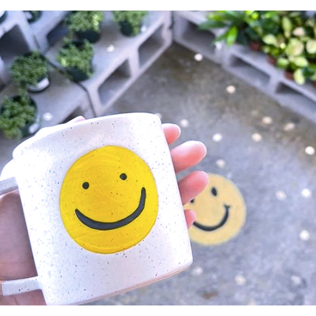 A white mug featuring a cheerful, smiling face design, perfect for adding a touch of positivity to your morning routine.