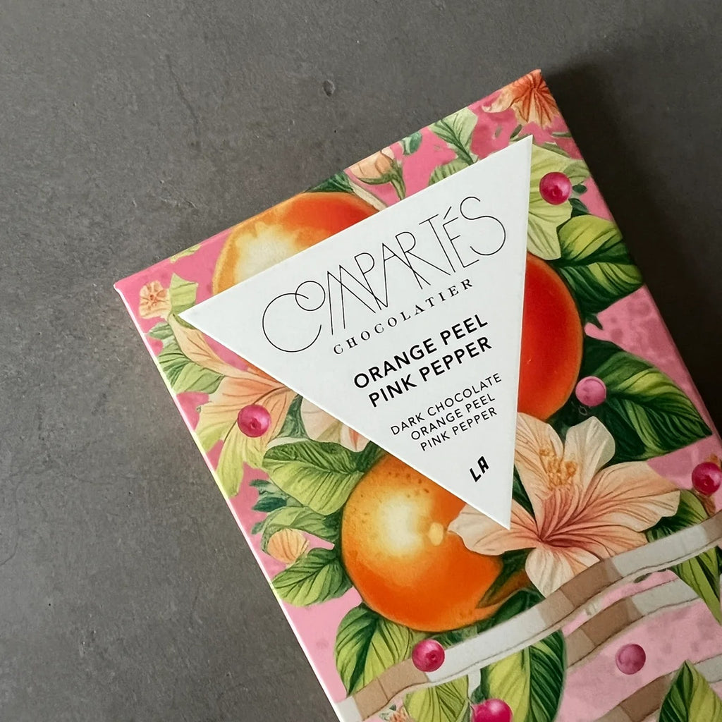 A dark chocolate bar with a rich texture, featuring pieces of orange peel and a hint of pink pepper for a unique and flavorful combination.